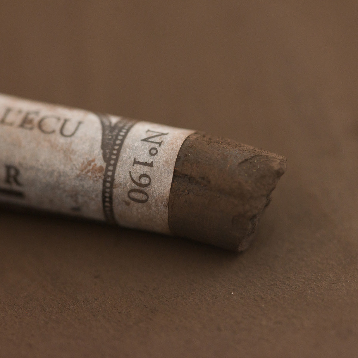 A close-up of a brown Sennelier extra soft pastel with the colour information printed on the paper wrap.