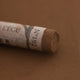 A close-up of a brown Sennelier extra soft pastel with the colour information printed on the paper wrap.