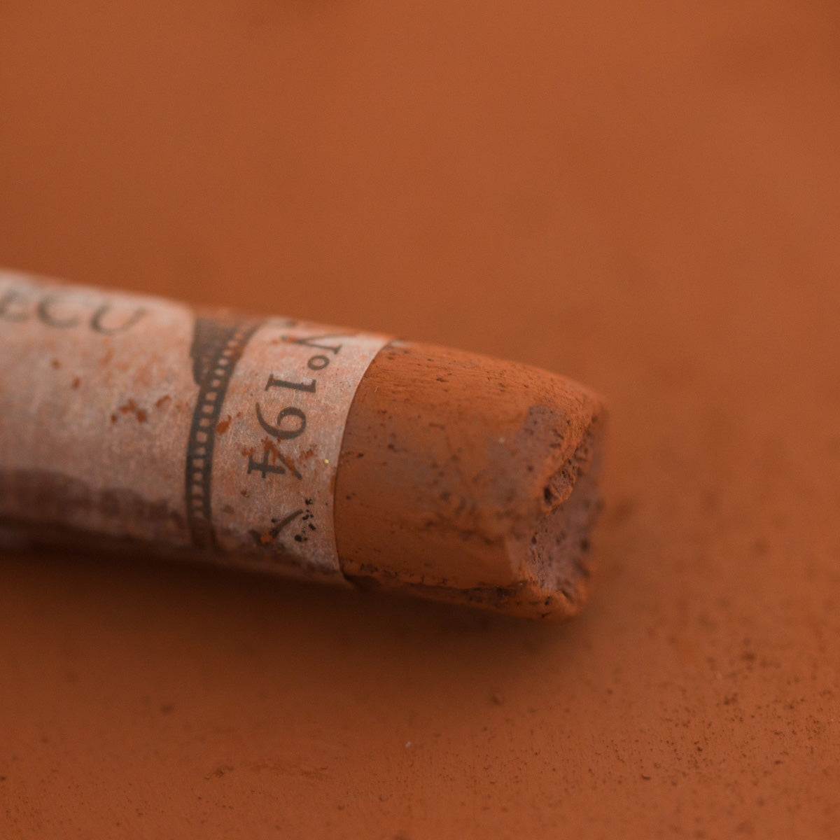 A close-up of a brown Sennelier extra soft pastel with the colour information printed on the paper wrap.