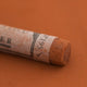 A close-up of a brown Sennelier extra soft pastel with the colour information printed on the paper wrap.