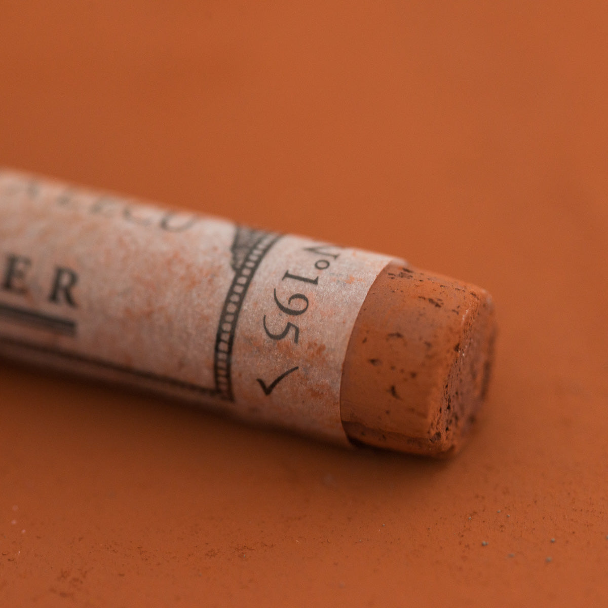 A close-up of a brown Sennelier extra soft pastel with the colour information printed on the paper wrap.