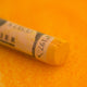 A close-up of an Orange Sennelier extra soft pastel. on the same coloured background, with the colour information printed on the paper wrap.