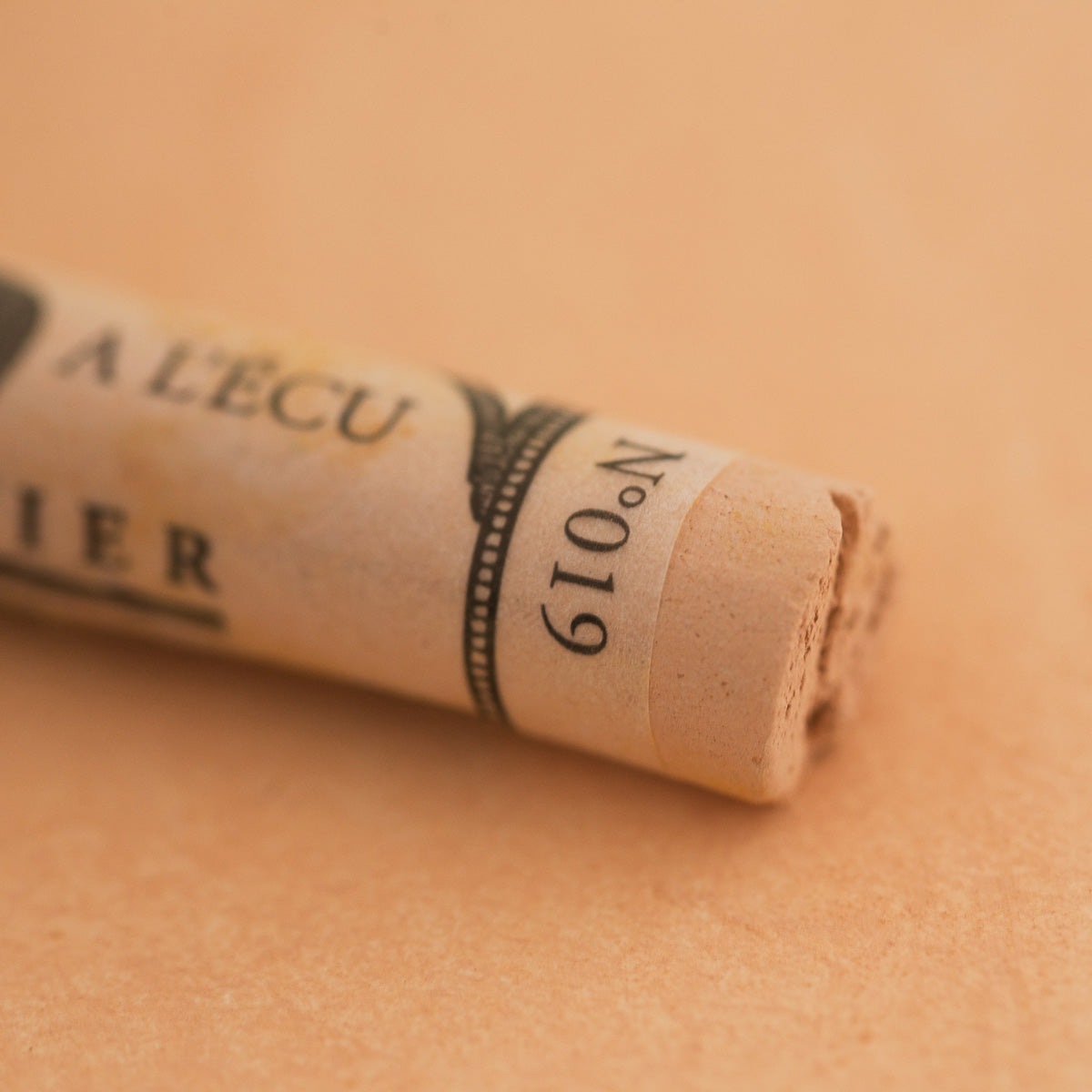 A close-up of a Sennelier extra soft pastel on a brown background with the colour information printed on the paper wrap.