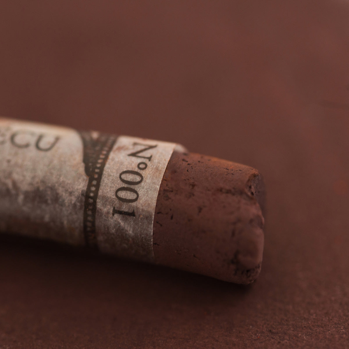 A close-up of a brown Sennelier extra soft pastel with the colour information printed on the paper wrap.