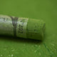 A close-up of a green Sennelier extra soft pastel, on the same coloured background, with the colour information printed on the paper wrap.