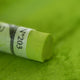A close-up of a bright green Sennelier extra soft pastel, on the same coloured background, with the colour information printed on the paper wrap.