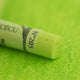 A close-up of a green Sennelier extra soft pastel. on the same coloured background, with the colour information printed on the paper wrap.