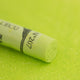 A close-up of a bright green Sennelier extra soft pastel. on the same coloured background, with the colour information printed on the paper wrap.