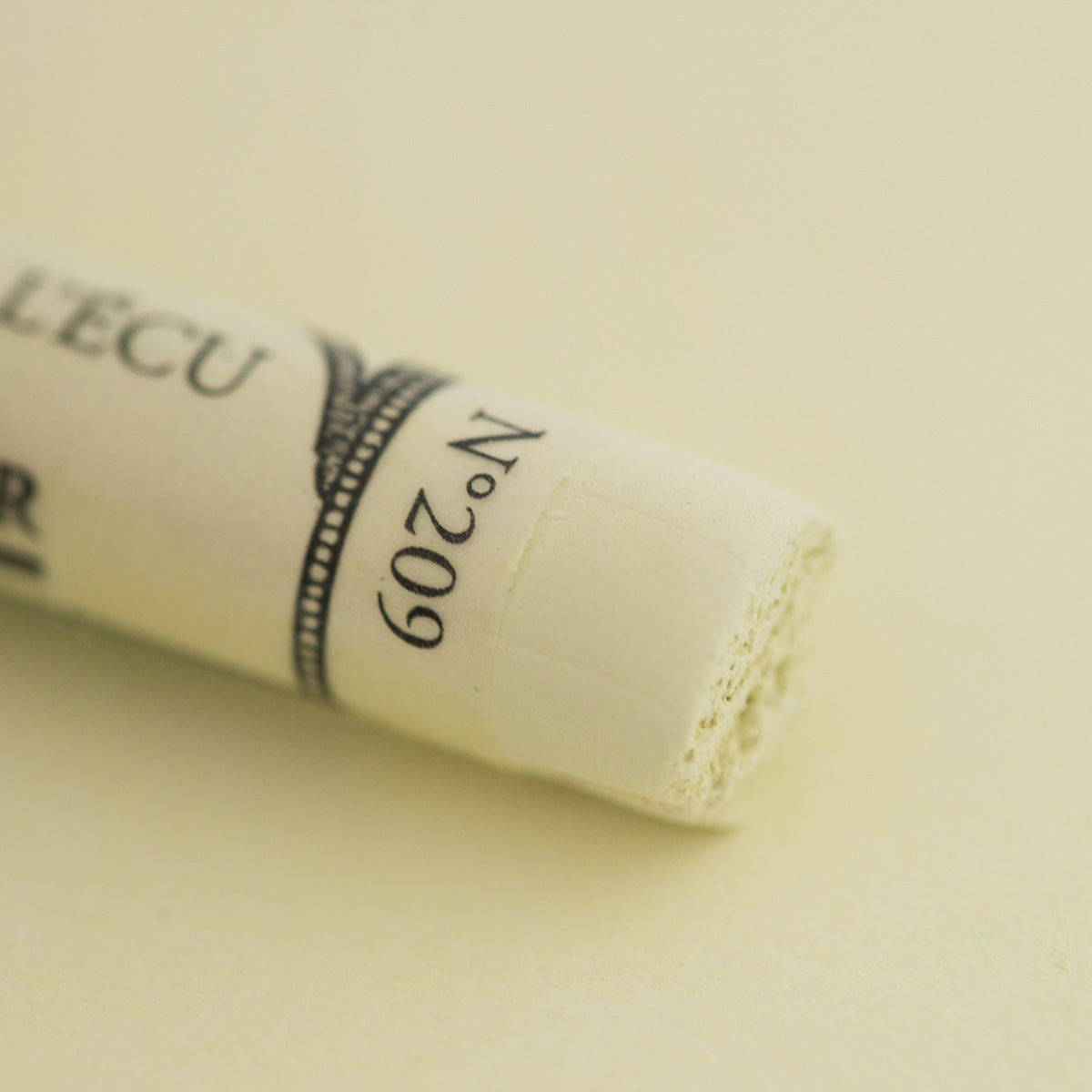 A close-up of a white Sennelier extra soft pastel. on the same coloured background, with the colour information printed on the paper wrap.