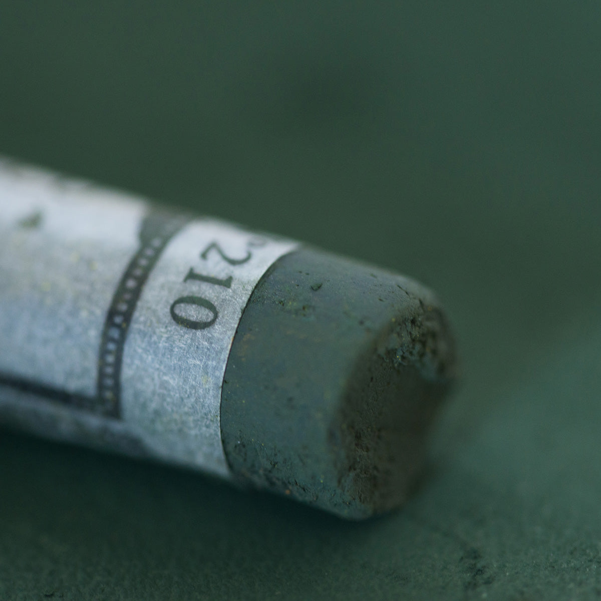 A close-up of a grey Sennelier extra soft pastel. on the same coloured background, with the colour information printed on the paper wrap.