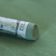 A close-up of a grey-green Sennelier extra soft pastel. on the same coloured background, with the colour information printed on the paper wrap.