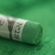 A close-up of a green Sennelier extra soft pastel, on the same coloured background, with the colour information printed on the paper wrap.