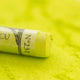 A close-up of a bright yellow-green Sennelier extra soft pastel, on the same coloured background, with the colour information printed on the paper wrap.
