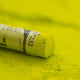 A close-up of a green Sennelier extra soft pastel, on the same coloured background, with the colour information printed on the paper wrap.