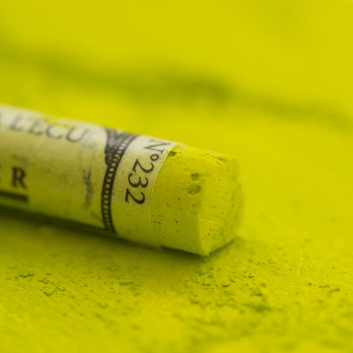 A close-up of a green Sennelier extra soft pastel, on the same coloured background, with the colour information printed on the paper wrap.