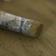 A close-up of a brown Sennelier extra soft pastel, on the same coloured background, with the colour information printed on the paper wrap.