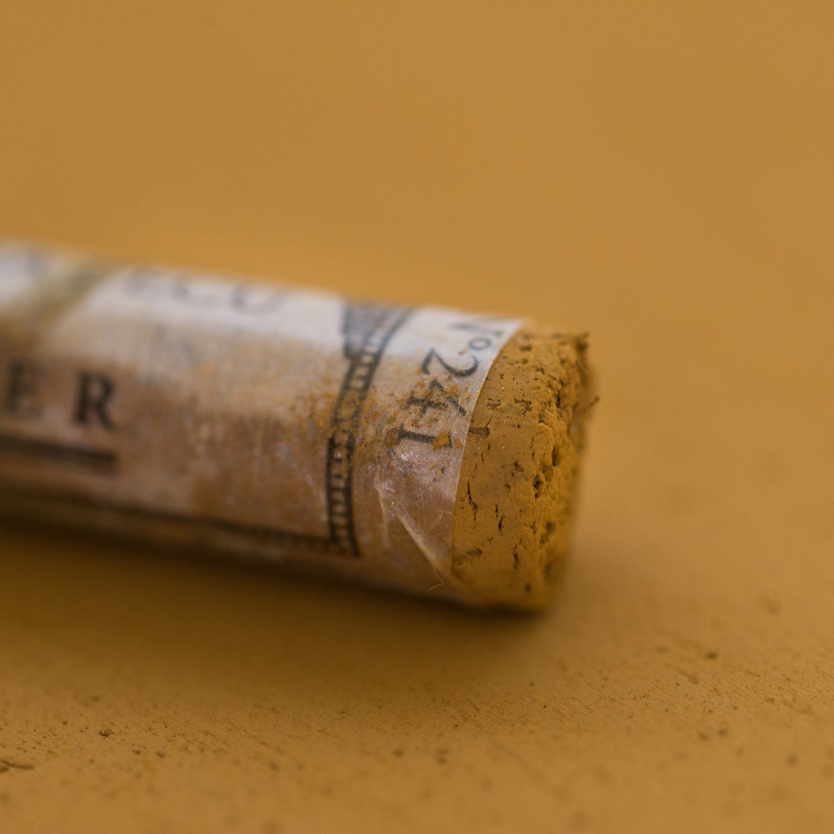 A close-up of a brown Sennelier extra soft pastel, on the same coloured background, with the colour information printed on the paper wrap.