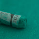 A close-up of a green Sennelier extra soft pastel. on the same coloured background, with the colour information printed on the paper wrap.
