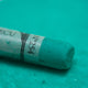 A close-up of a green Sennelier extra soft pastel. on the same coloured background, with the colour information printed on the paper wrap.