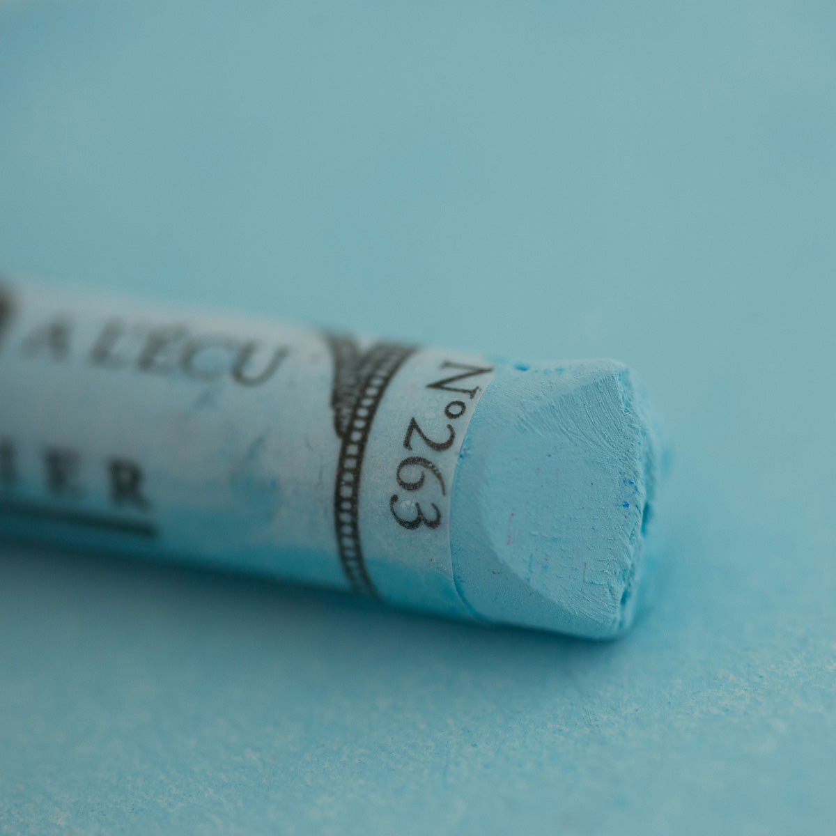 A close-up of a blue Sennelier extra soft pastel on the same coloured background, with the colour information printed on the paper wrap.