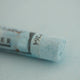 A close-up of a pale blue Sennelier extra soft pastel on the same coloured background, with the colour information printed on the paper wrap.