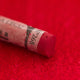 A close-up of a red Sennelier extra soft pastel on the same coloured background, with the colour information printed on the paper wrap.