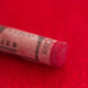 A close-up of a red Sennelier extra soft pastel on the same coloured background, with the colour information printed on the paper wrap.