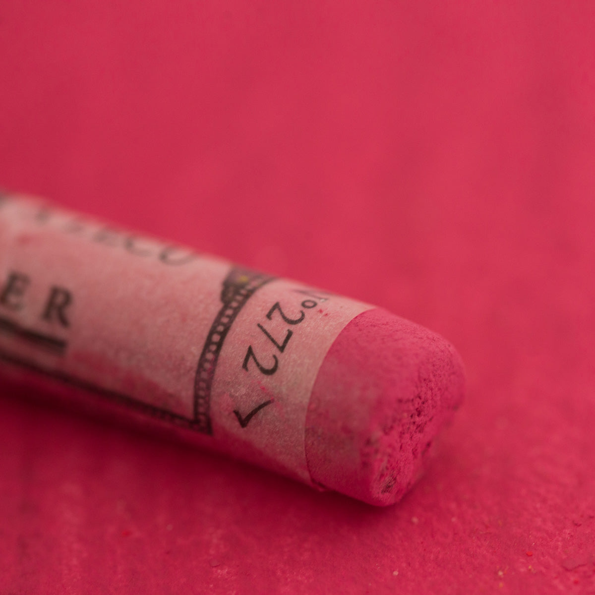 A close-up of a pink Sennelier extra soft pastel. on the same coloured background, with the colour information printed on the paper wrap.
