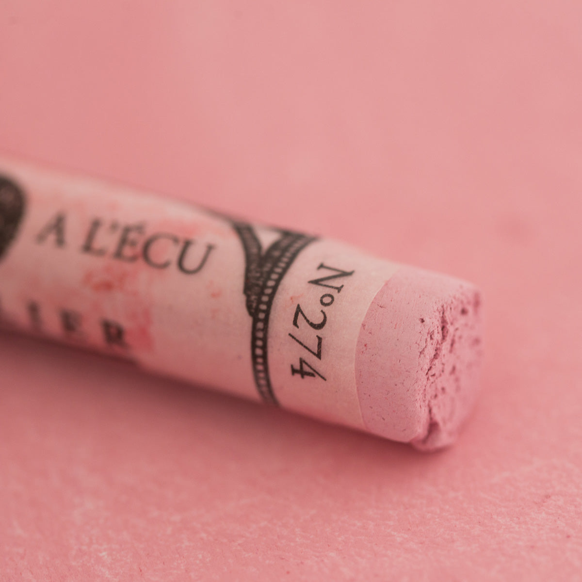 A close-up of a light pink Sennelier extra soft pastel. on the same coloured background, with the colour information printed on the paper wrap.