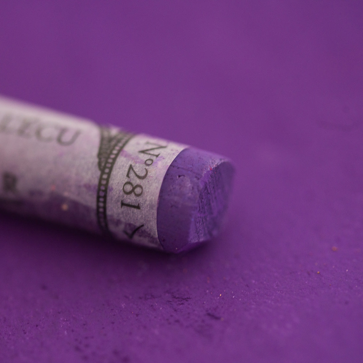  A close-up of a purple Sennelier extra soft pastel on the same coloured background, with the colour information printed on the paper wrap.