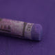  A close-up of a purple Sennelier extra soft pastel on the same coloured background, with the colour information printed on the paper wrap.