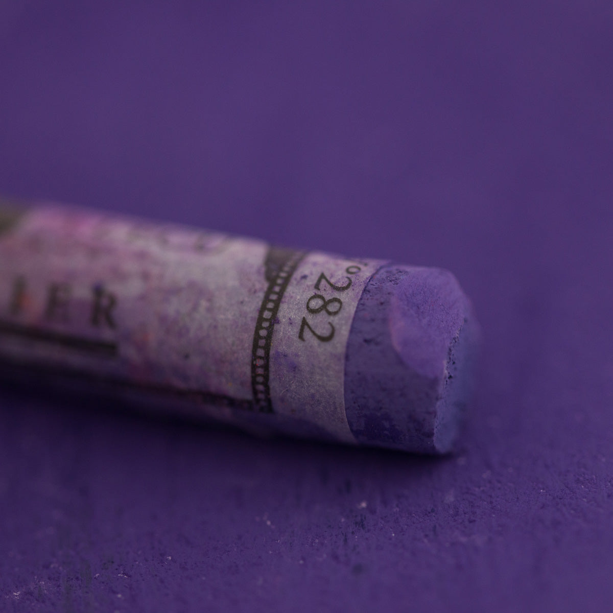  A close-up of a purple Sennelier extra soft pastel on the same coloured background, with the colour information printed on the paper wrap.
