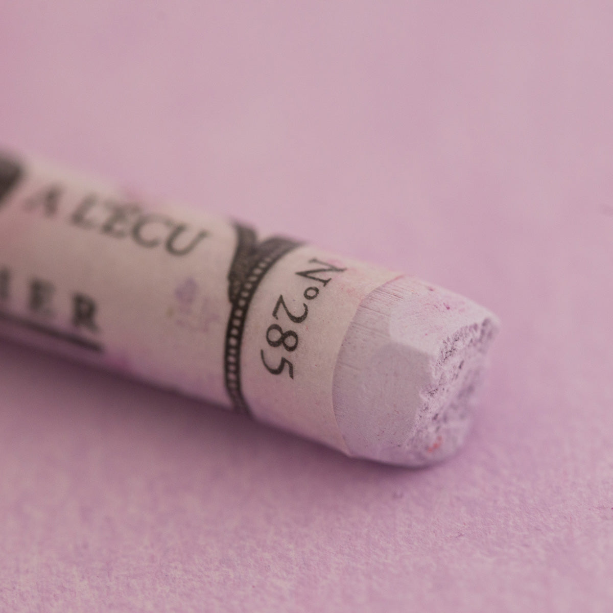  A close-up of a light purple Sennelier extra soft pastel on the same coloured background, with the colour information printed on the paper wrap.