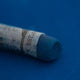 A close-up of a blue Sennelier extra soft pastel on the same coloured background, with the colour information printed on the paper wrap.