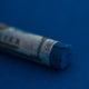 A close-up of a blue Sennelier extra soft pastel on the same coloured background, with the colour information printed on the paper wrap.
