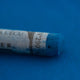 A close-up of a blue Sennelier extra soft pastel on the same coloured background, with the colour information printed on the paper wrap.