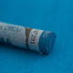 A close-up of a blue Sennelier extra soft pastel on the same coloured background, with the colour information printed on the paper wrap.