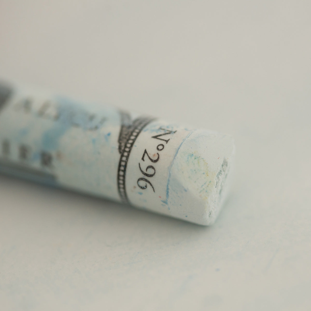 A close-up of a white Sennelier extra soft pastel on the same coloured background, with the colour information printed on the paper wrap.
