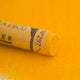 A close-up of a deep yellow Sennelier extra soft pastel. on the same coloured background, with the colour information printed on the paper wrap.