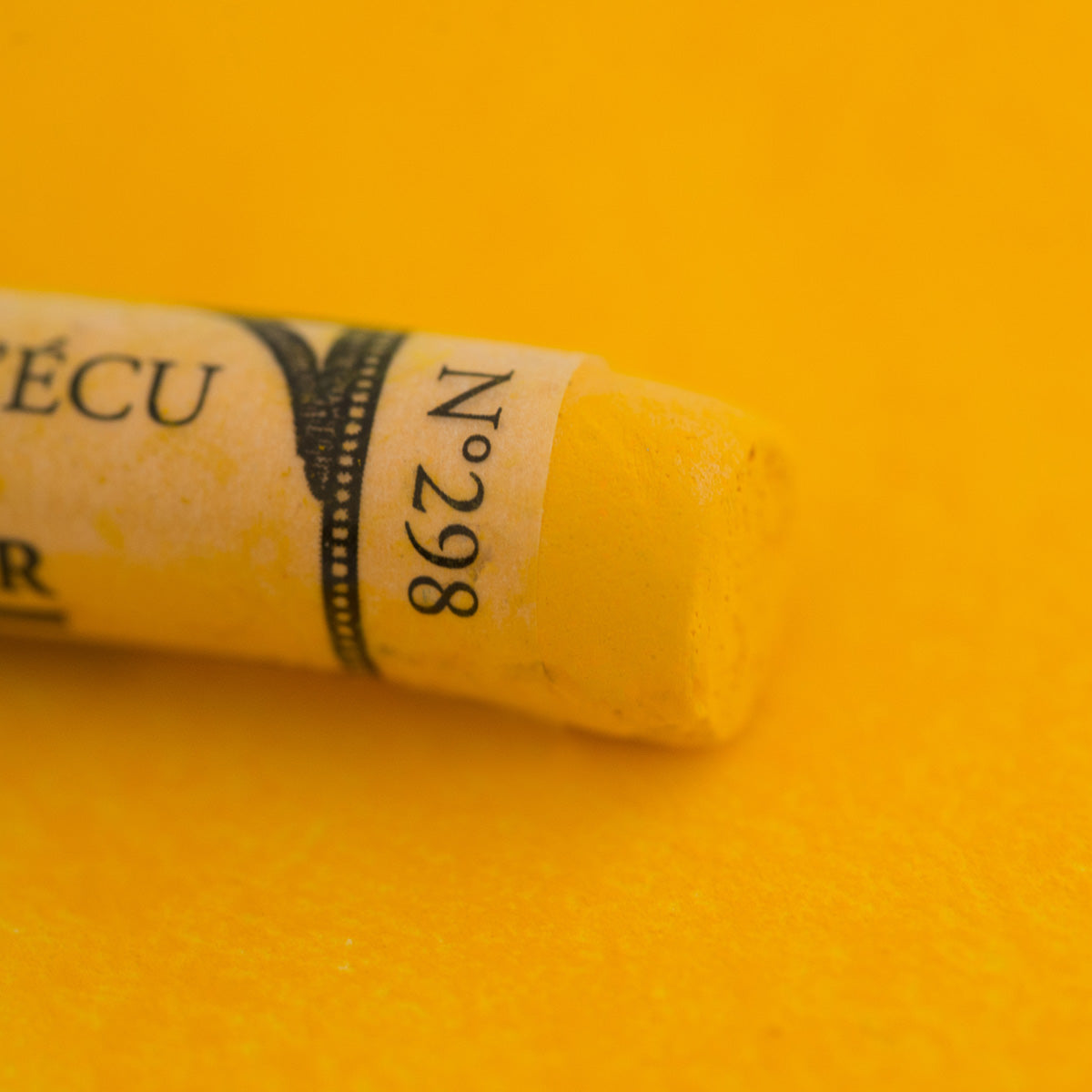 A close-up of a yellow Sennelier extra soft pastel. on the same coloured background, with the colour information printed on the paper wrap.