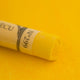 A close-up of a vibrant yellow Sennelier extra soft pastel. on the same coloured background, with the colour information printed on the paper wrap.