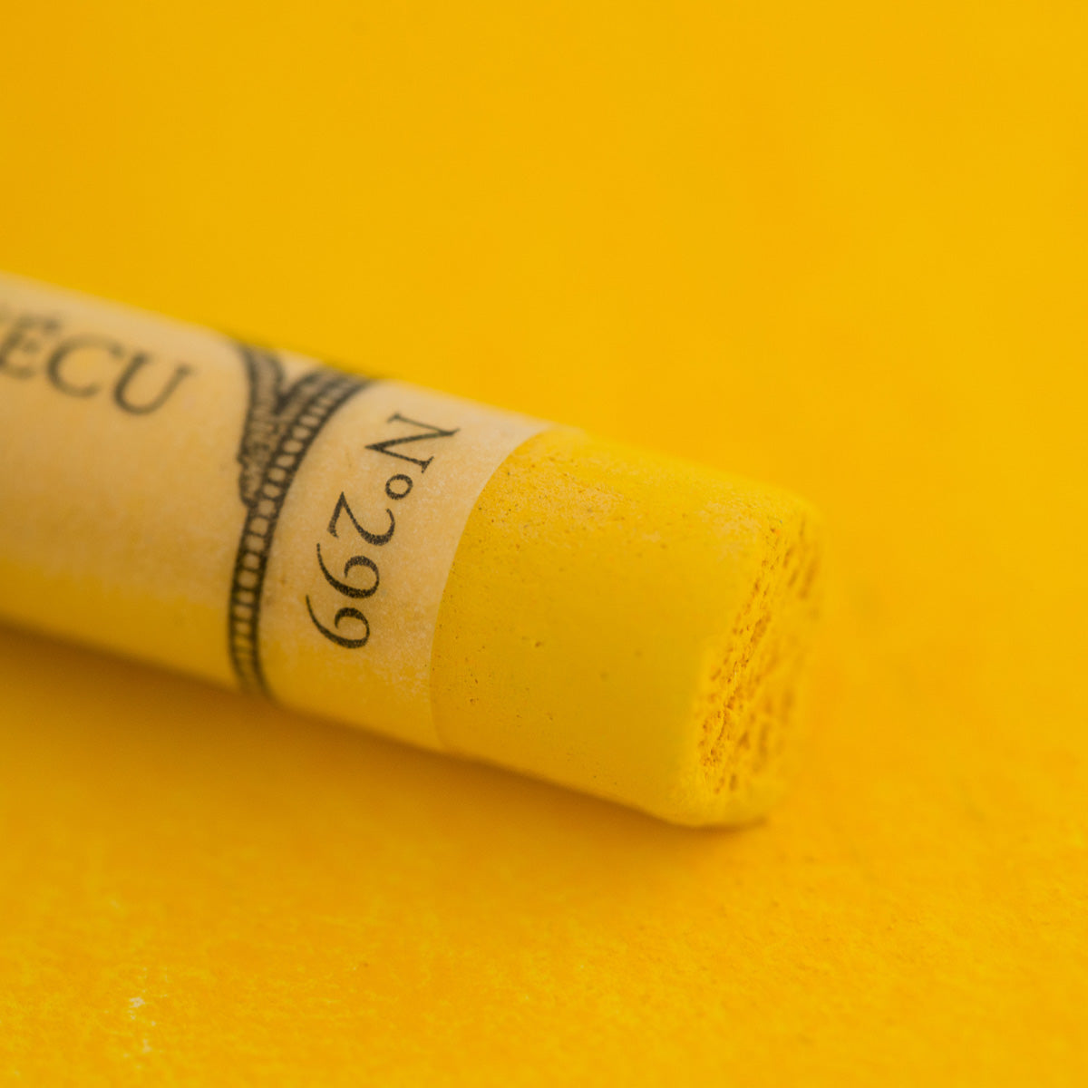 A close-up of a vibrant yellow Sennelier extra soft pastel. on the same coloured background, with the colour information printed on the paper wrap.
