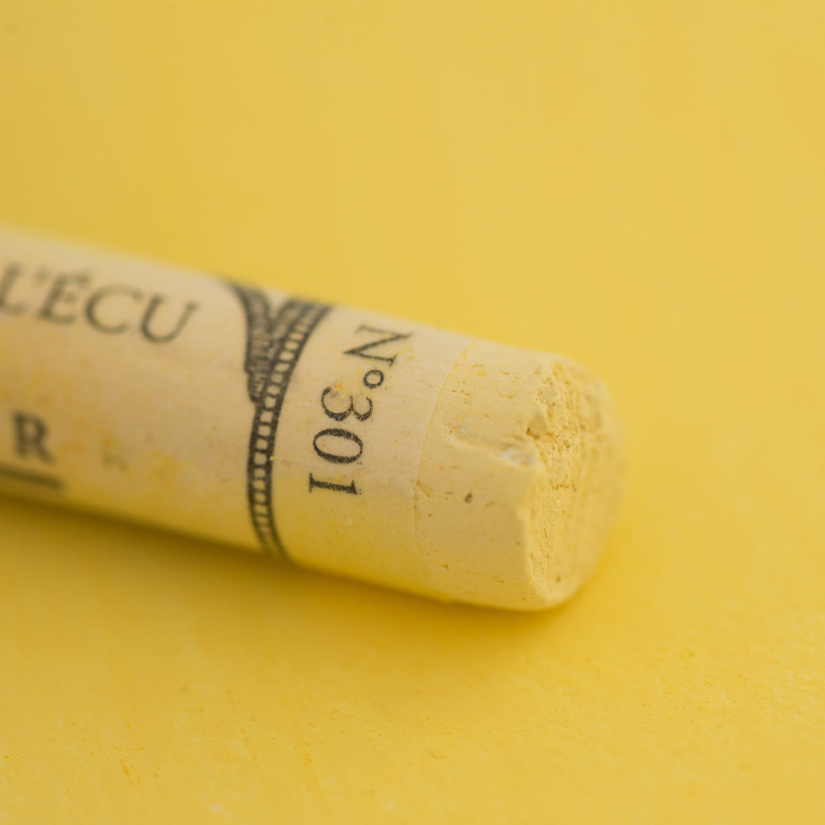 A close-up of a light yellow Sennelier extra soft pastel. on the same coloured background, with the colour information printed on the paper wrap.