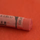 A close-up of a red Sennelier extra soft pastel on the same coloured background, with the colour information printed on the paper wrap.