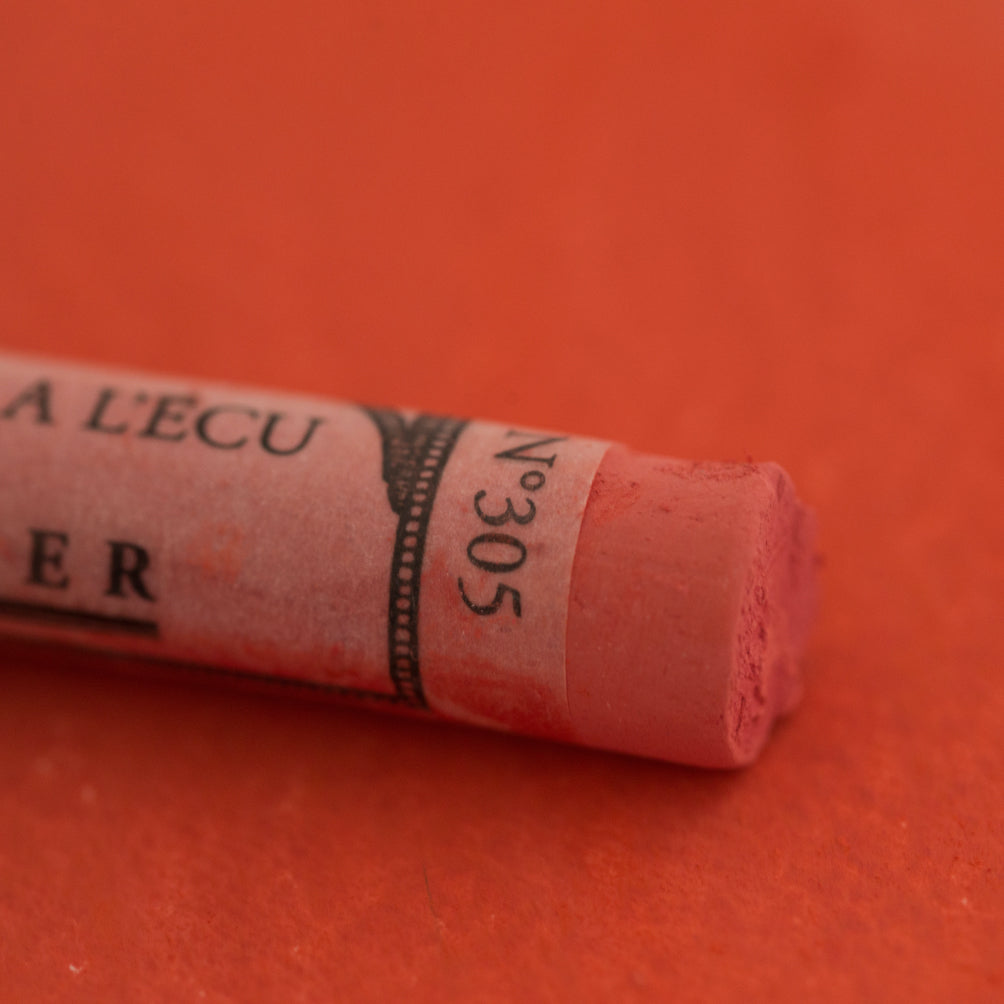 A close-up of a red Sennelier extra soft pastel on the same coloured background, with the colour information printed on the paper wrap.