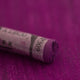 A close-up of a purple Sennelier extra soft pastel on the same coloured background, with the colour information printed on the paper wrap.