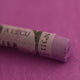 A close-up of a purple Sennelier extra soft pastel. on the same coloured background, with the colour information printed on the paper wrap.