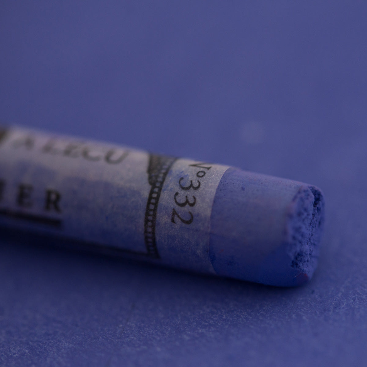  A close-up of a blue Sennelier extra soft pastel on the same coloured background, with the colour information printed on the paper wrap.