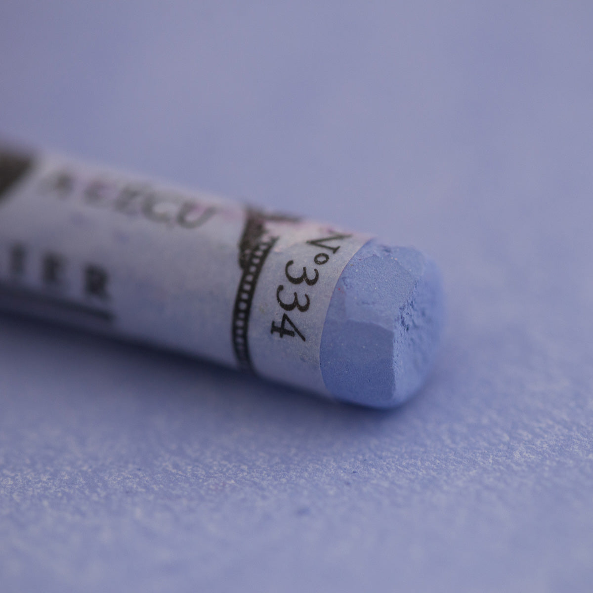  A close-up of a light blue Sennelier extra soft pastel on the same coloured background, with the colour information printed on the paper wrap.