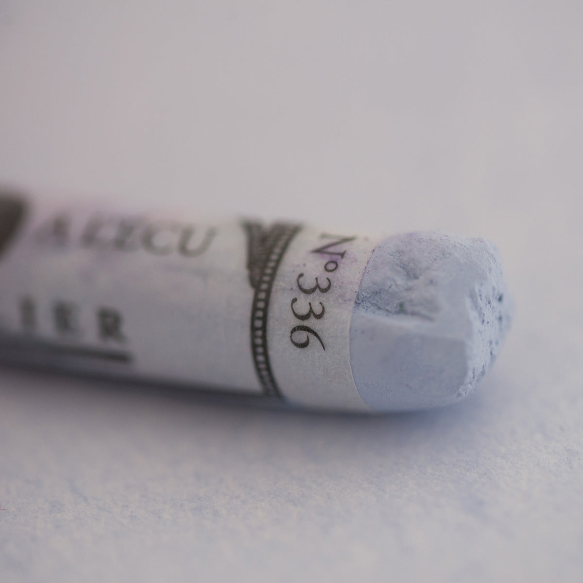  A close-up of a white Sennelier extra soft pastel on the same coloured background, with the colour information printed on the paper wrap.